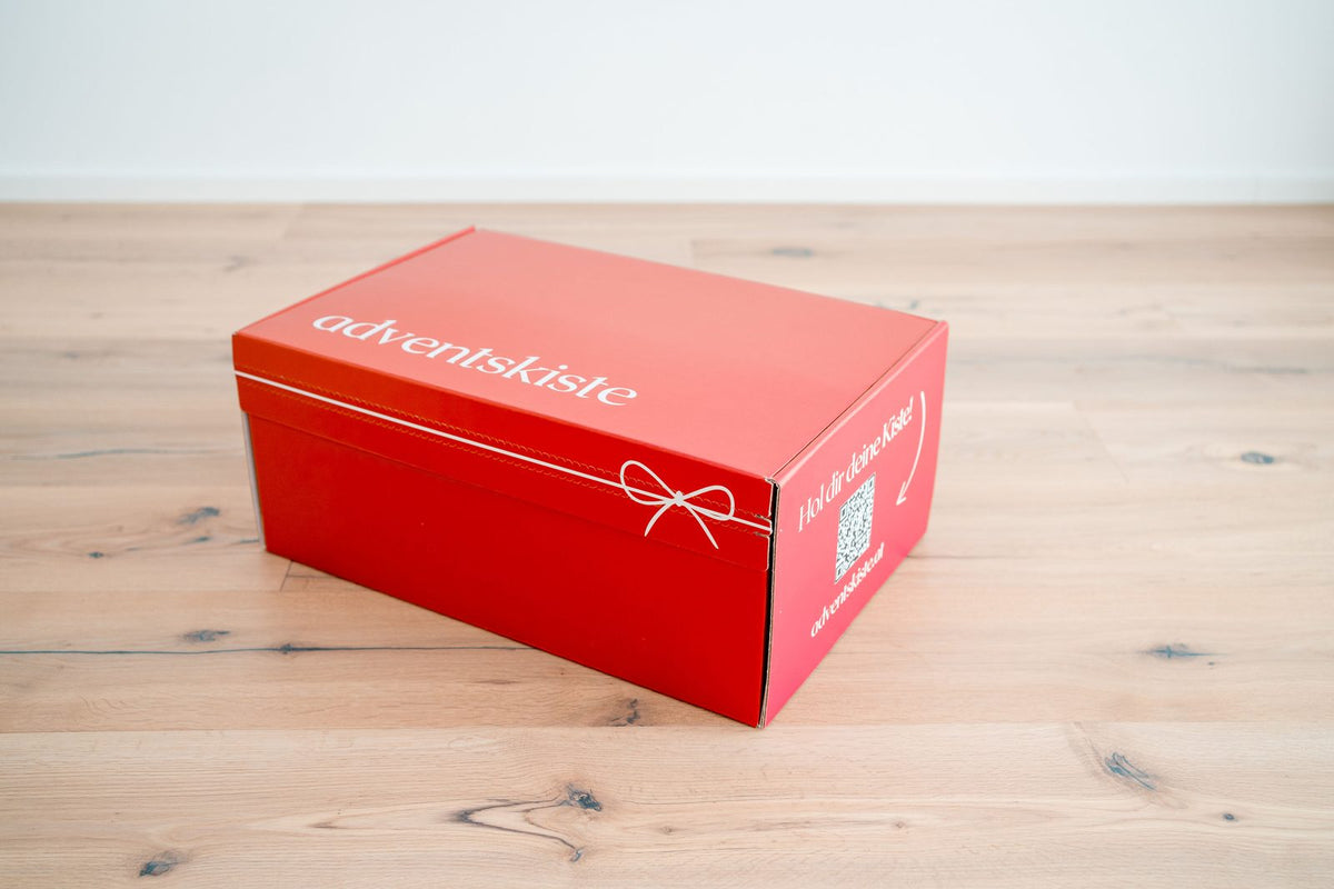 Geschlossene rote Adventkiste mit weißem Schriftzug adventskiste und aufgedruckter Schleife.